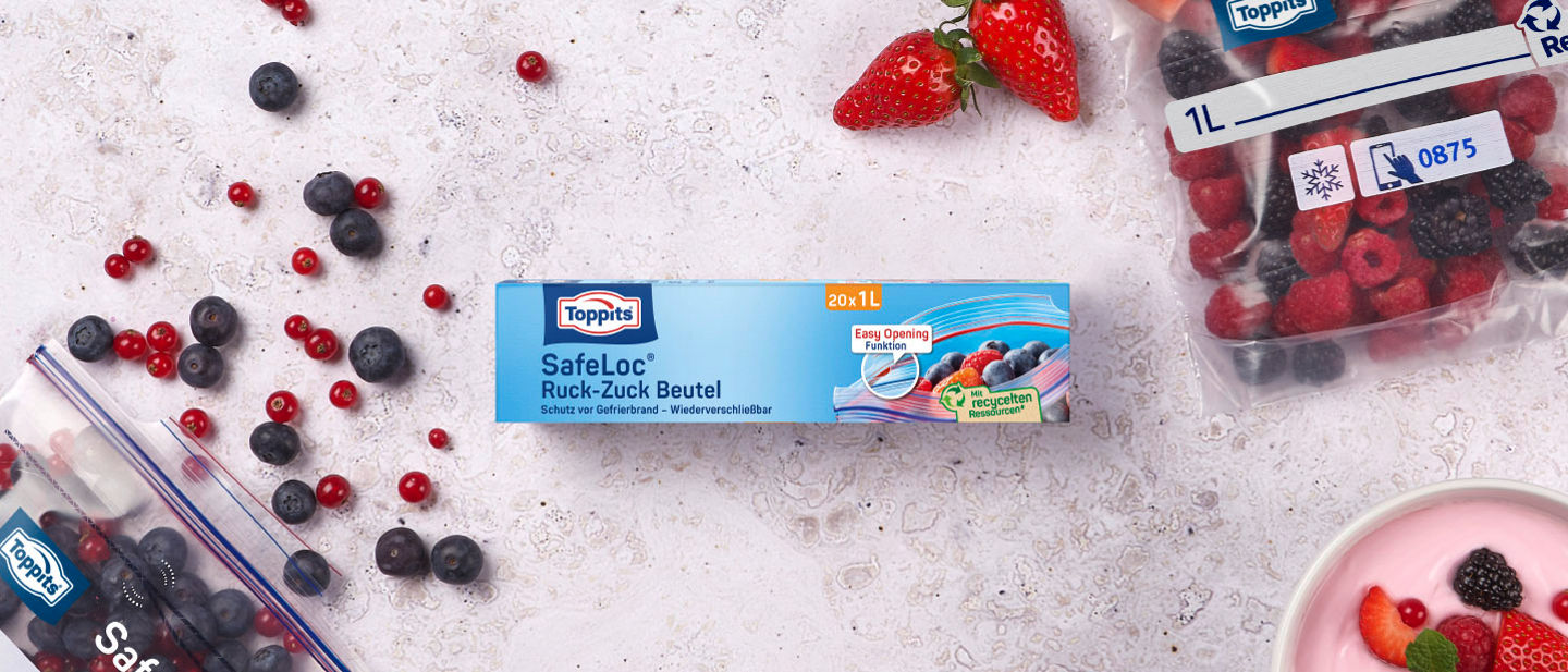 Toppits SafeLoc Ruck-Zuck Beutel (20 x 1L) auf Tisch, umgeben von Beeren, Joghurt und gefüllten SafeLoc Ruck- Zuck Beuteln