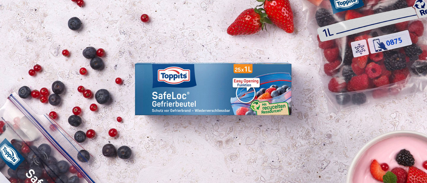 Toppits SafeLoc Gefrierbeutel (25 x 1L) auf Tisch, umgeben von Beeren, Joghurt und gefüllten SafeLoc Gefrierbeuteln