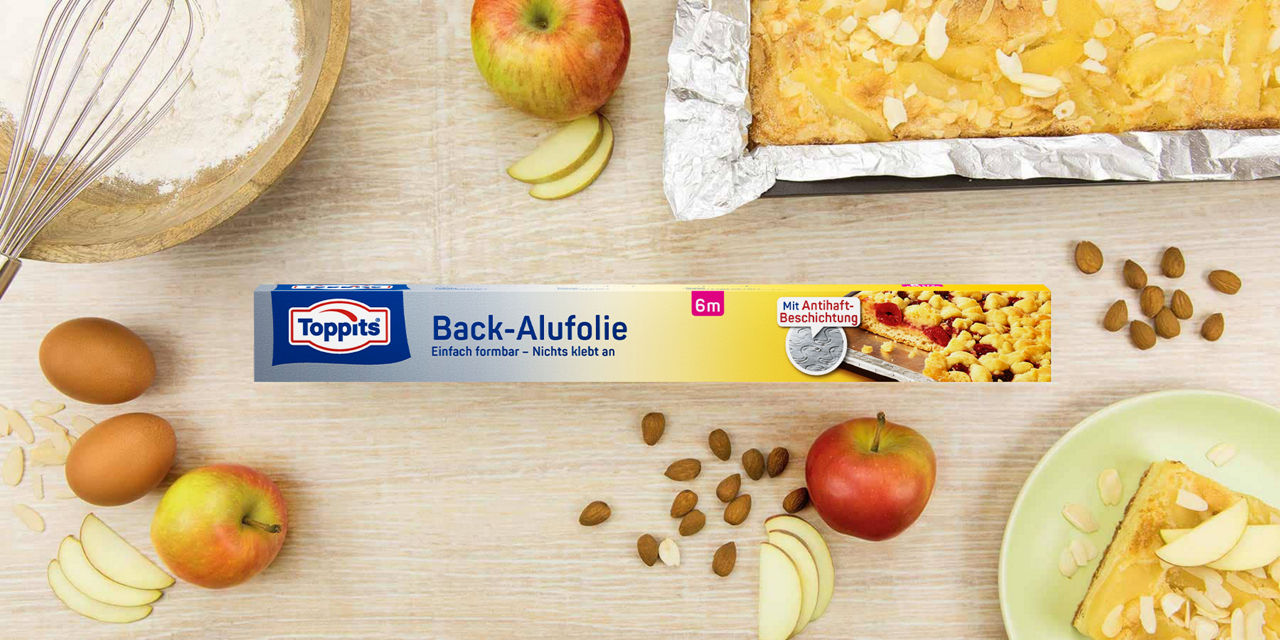 Toppits Back-Alufolie Verpackung mit Apfelkuchen, Mandeln und Backzutaten im Hintergrund.
