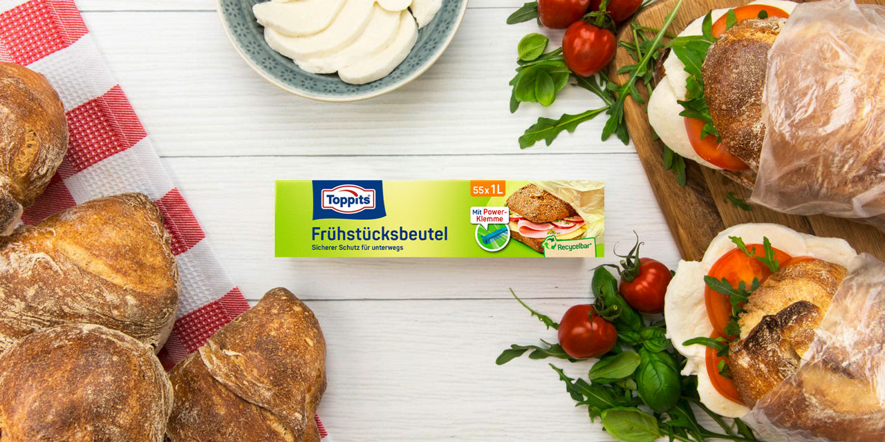 Toppits Frühstücksbeutel neben frischen Brötchen, Tomaten, Basilikum und Mozzarella auf Holzbrett.