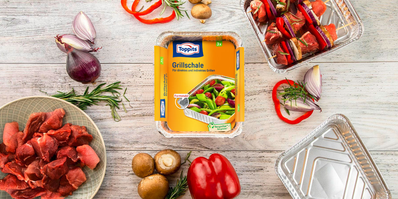Toppits Grillschale mit frischen Zutaten, Fleischspießen und Gemüse auf einer Holzoberfläche.