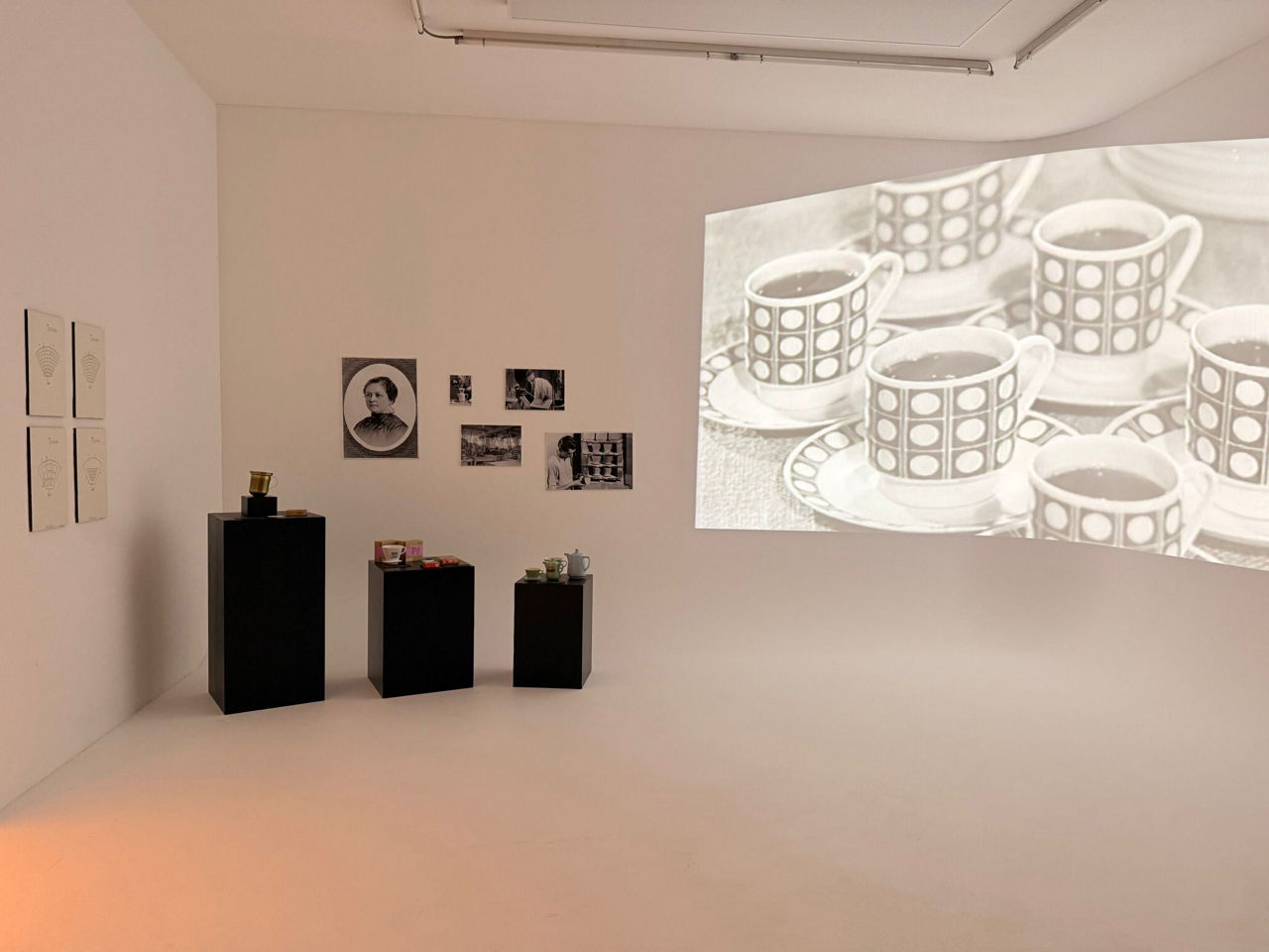 Heller, leerer Raum mit einer großen Projektion einer Kaffeemaschinen-Illustration an der Wand; auf dem Boden stehen schwarze Kaffeemaschinen auf Sockeln. 