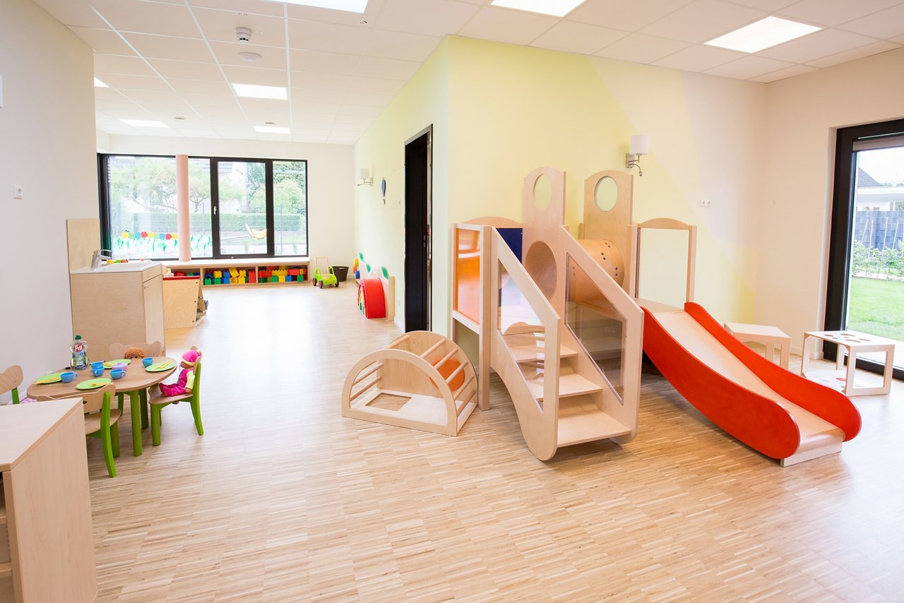 A bright play area with wooden flooring in the daycare center with wooden climbing frame with red slide,
