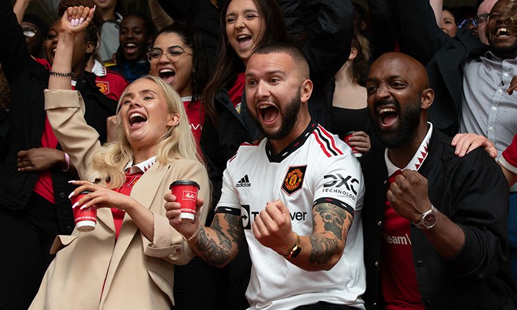 Melitta® ManUnited Fans Fans celebrating in the grandstand in the stadium holding a Melitta coffee cup 
