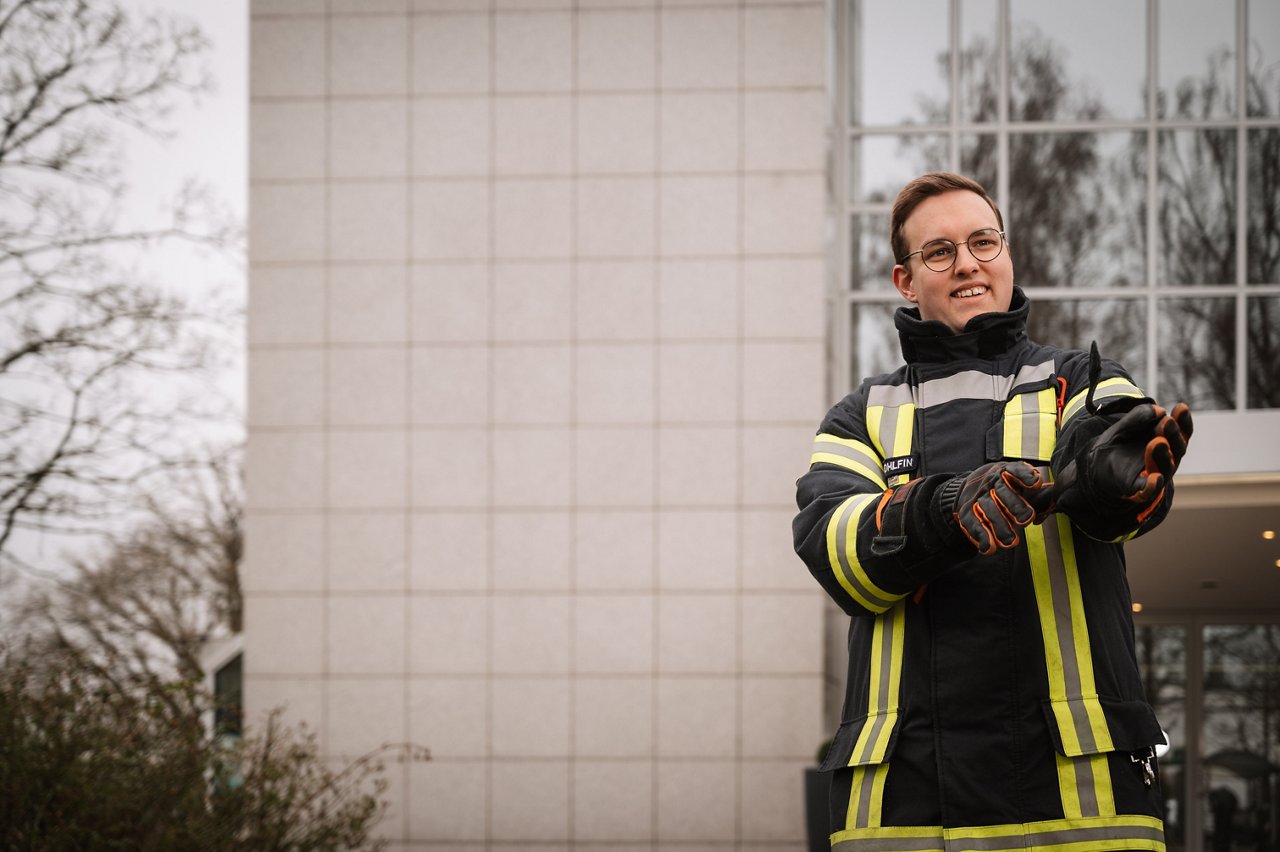Male person in firefighter suit standing with crossed arms in front of Melitta company headquarters and smiling at camera