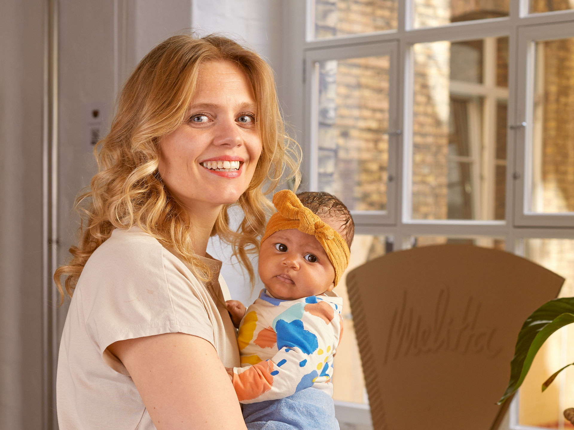 Eine blonde Frau in pinken Anzug lächelt und hält ein Baby in der Hand.