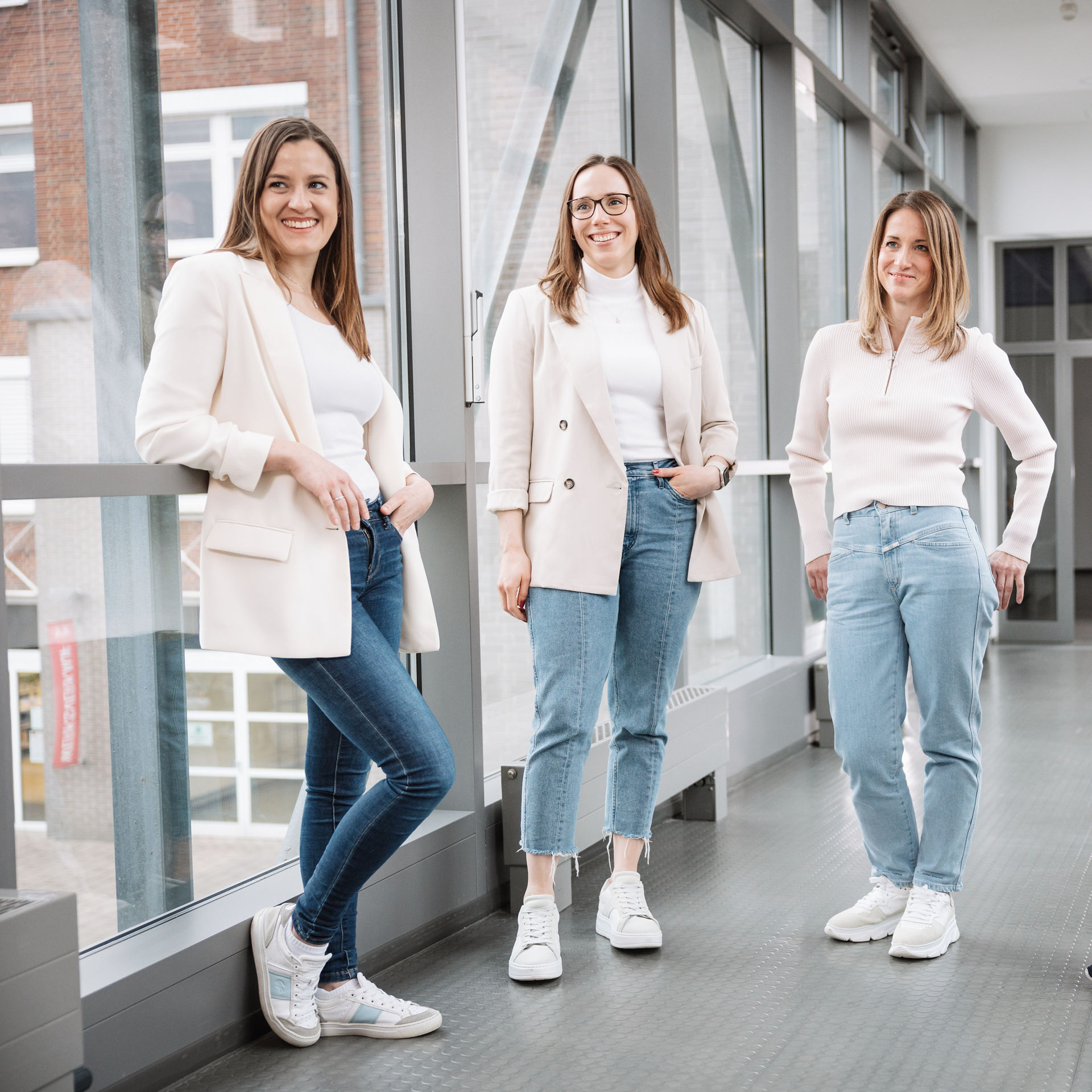 Four women, recruiters at Melitta, stand in a light corridor between two buildings and smile at the camera