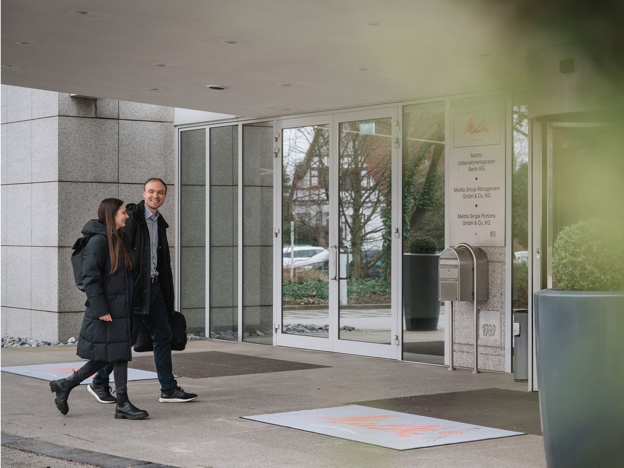 A young woman and a young man walk together into an office building.