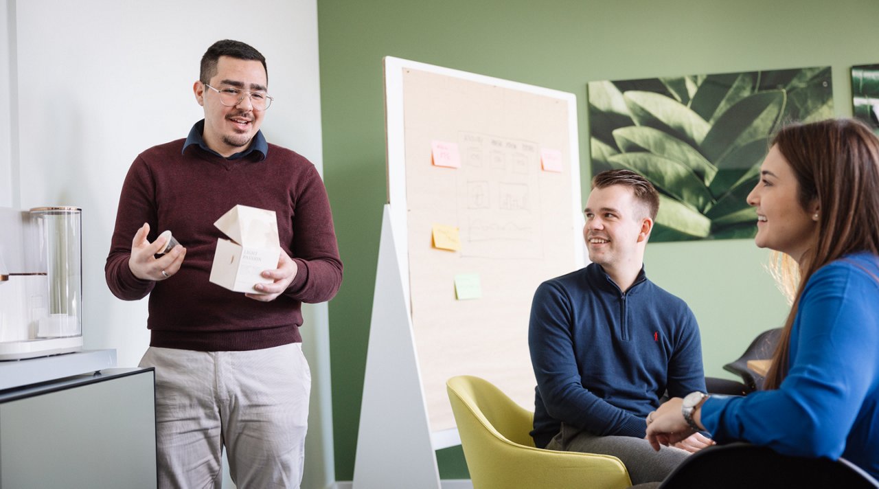 Drei Kollegen, zwei Männer und eine Frau unterhalten sich im Büro