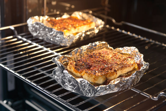 Zwei Stücke gewürzter Fisch liegen in Toppits Alufolie eingewickelt auf einem Rost im Backofen und werden gegart