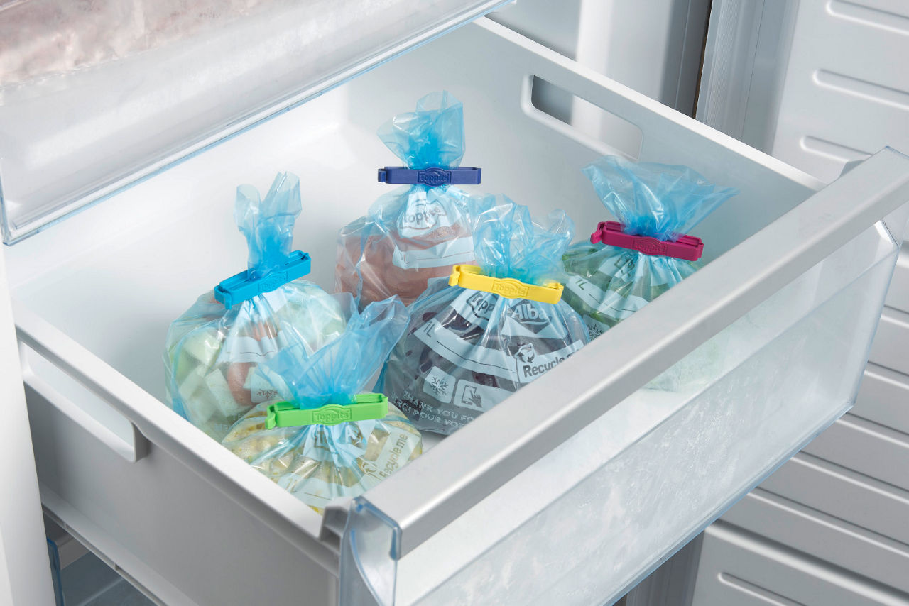 Fryslåda med flera blå fryspåsar, förslutna med färgglada klämmor, fyllda med olika livsmedel.