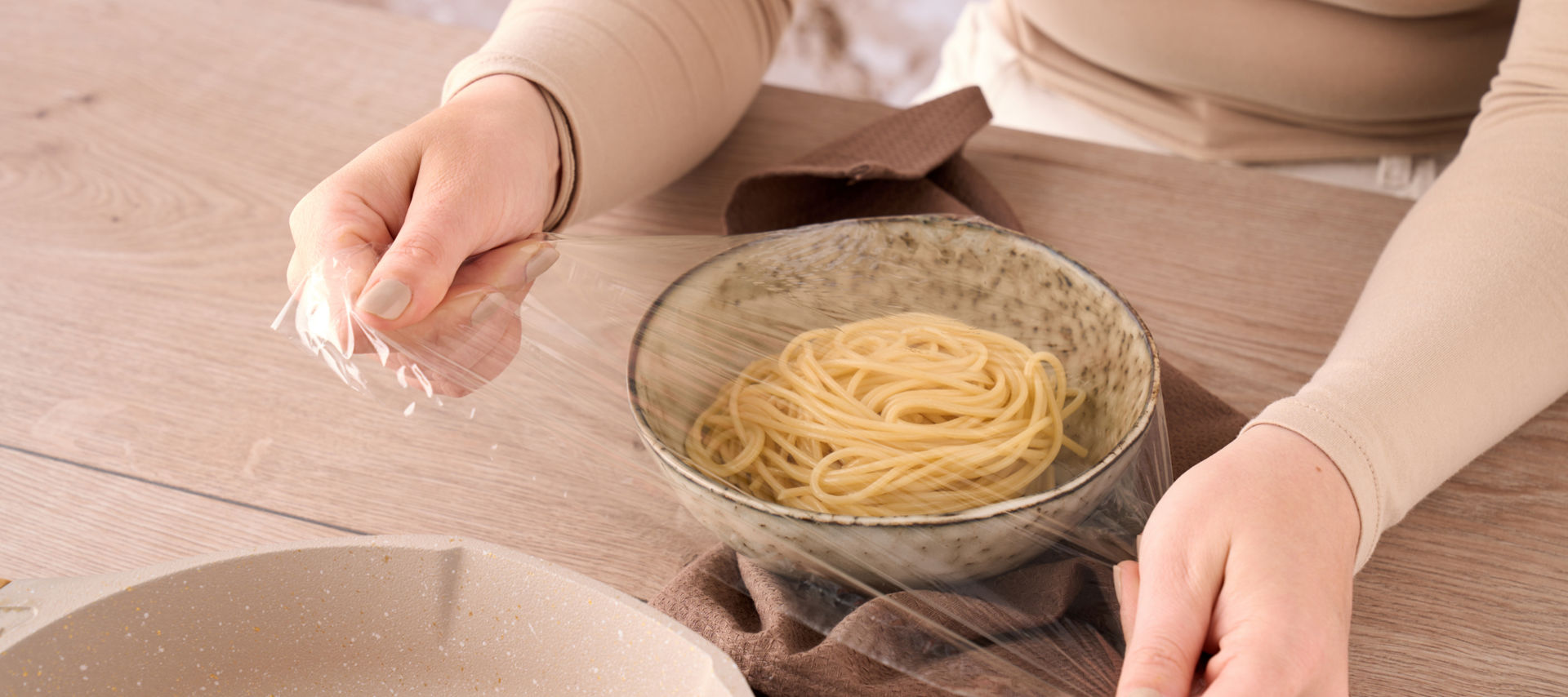 Person dekker en bolle med spaghetti med Toppits plastfolie.