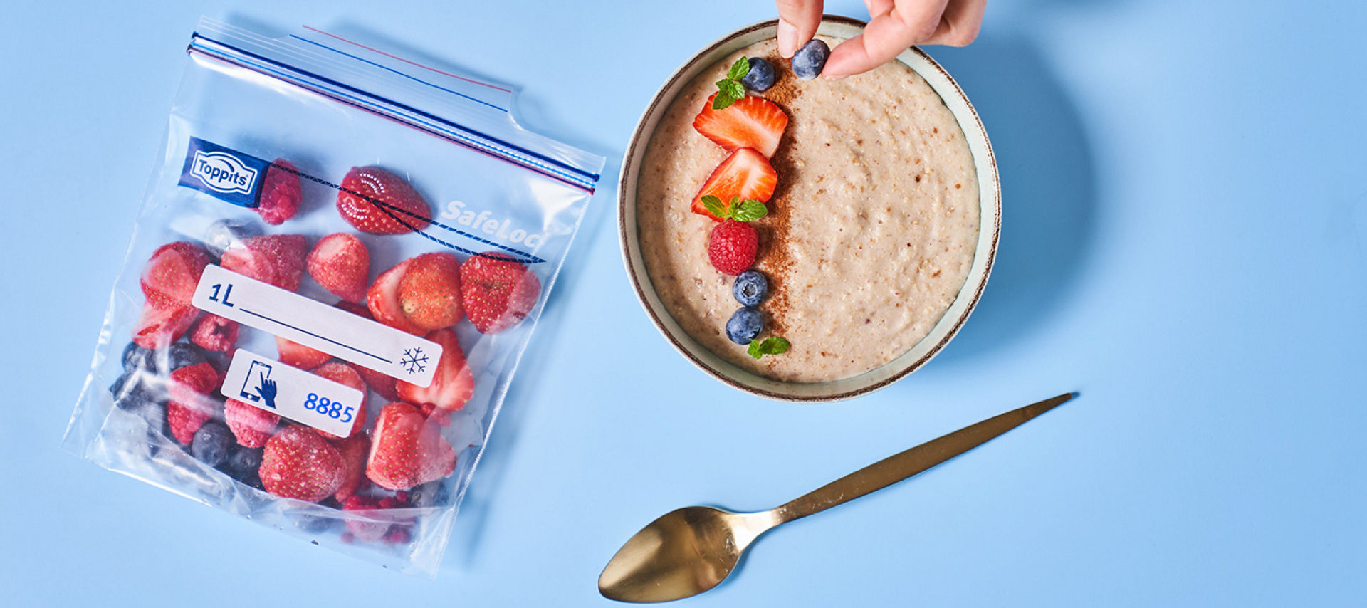  Toppits SafeLoc Gefrierbeutel mit gefrorenen Beeren neben einer Schale Porridge, die mit frischem Obst garniert wird. 