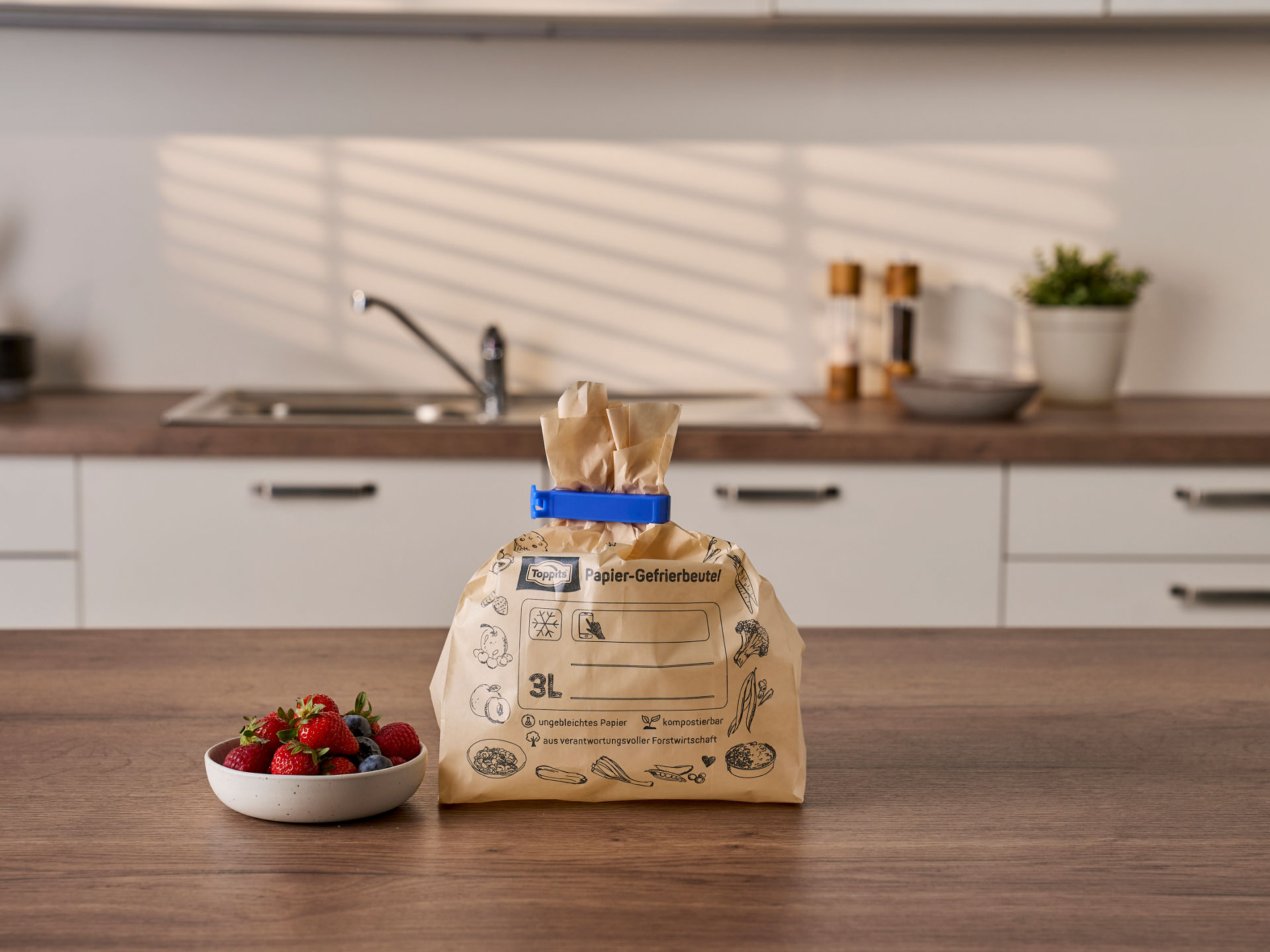 Ein verschlossener Toppits Papier-Gefrierbeutel steht in einer Küche neben einer Schale mit Beeren.