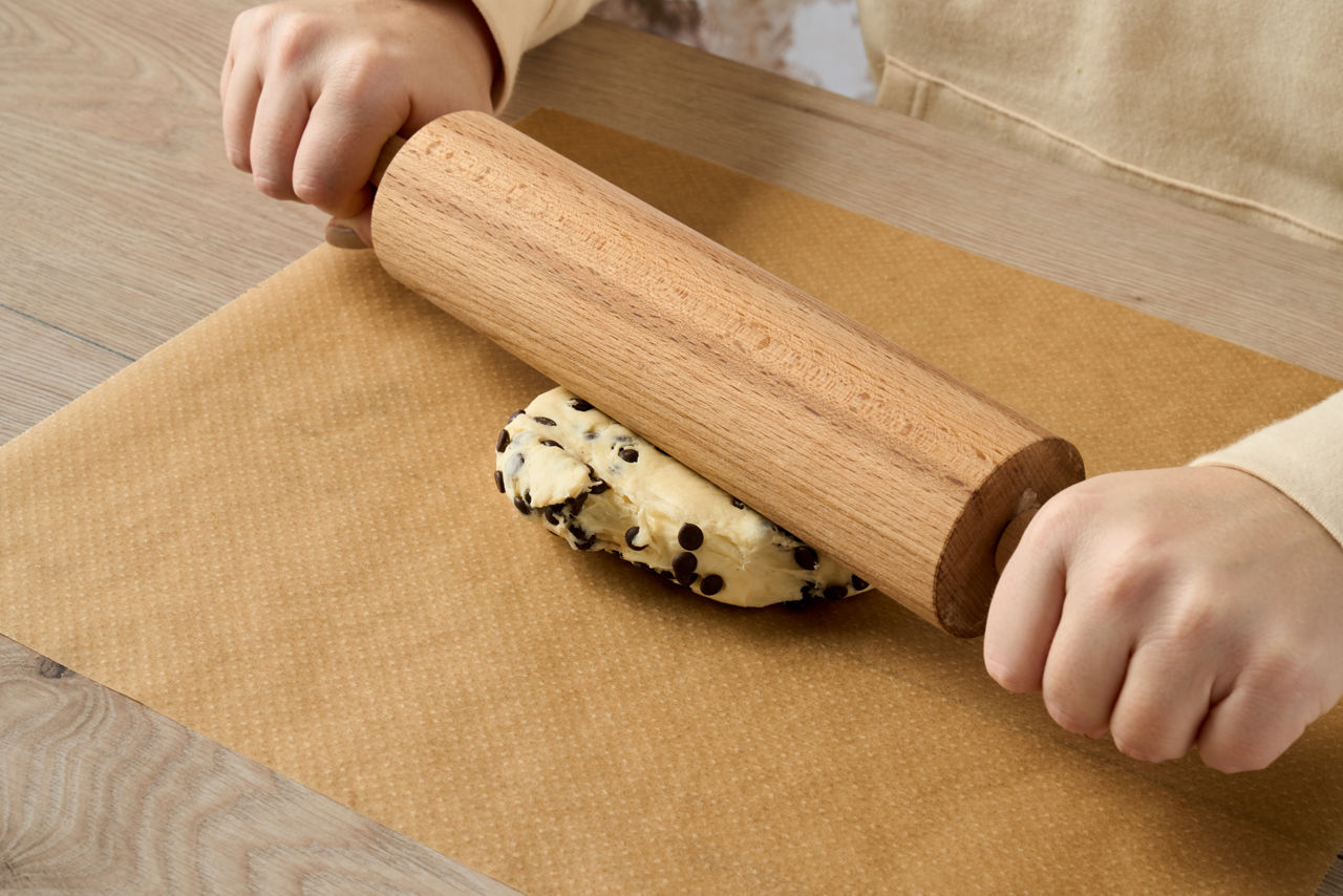  Pâte aux pépites de chocolat étalée sur du papier cuisson Albal® brun avec un rouleau à pâtisserie