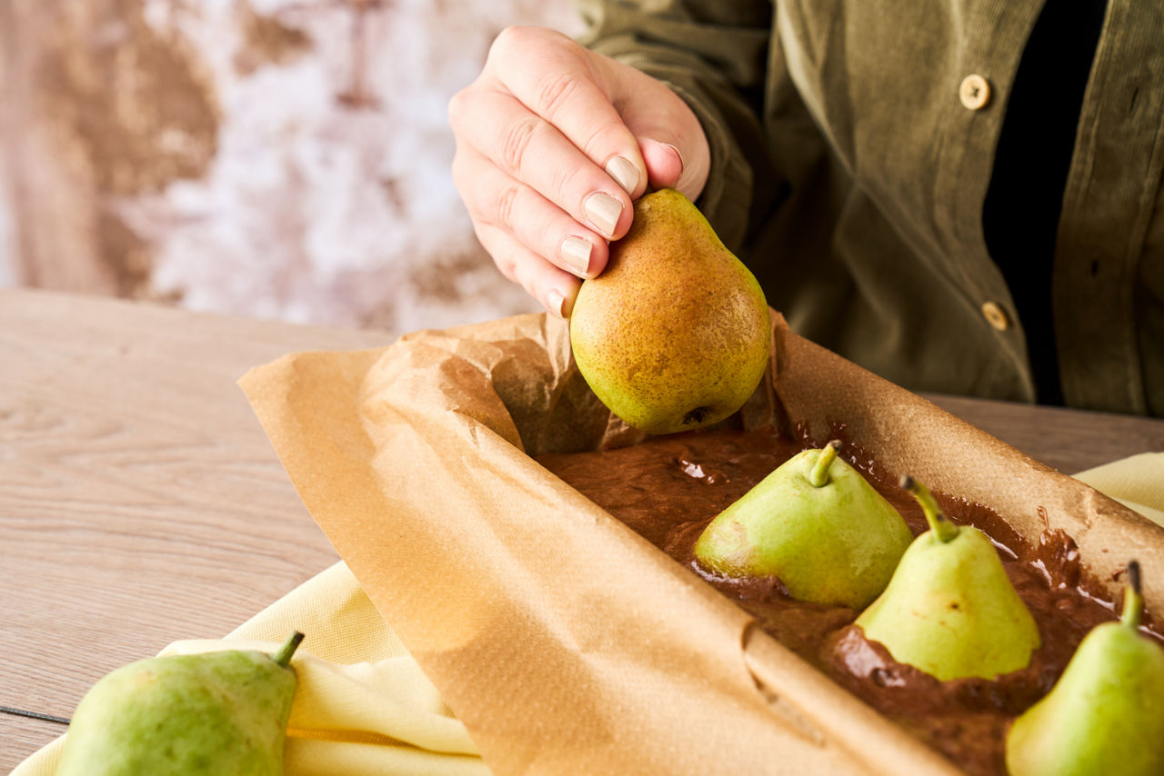 Poires déposées dans un moule à gâteau avec du papier sulfurisé et une préparation au chocolat
