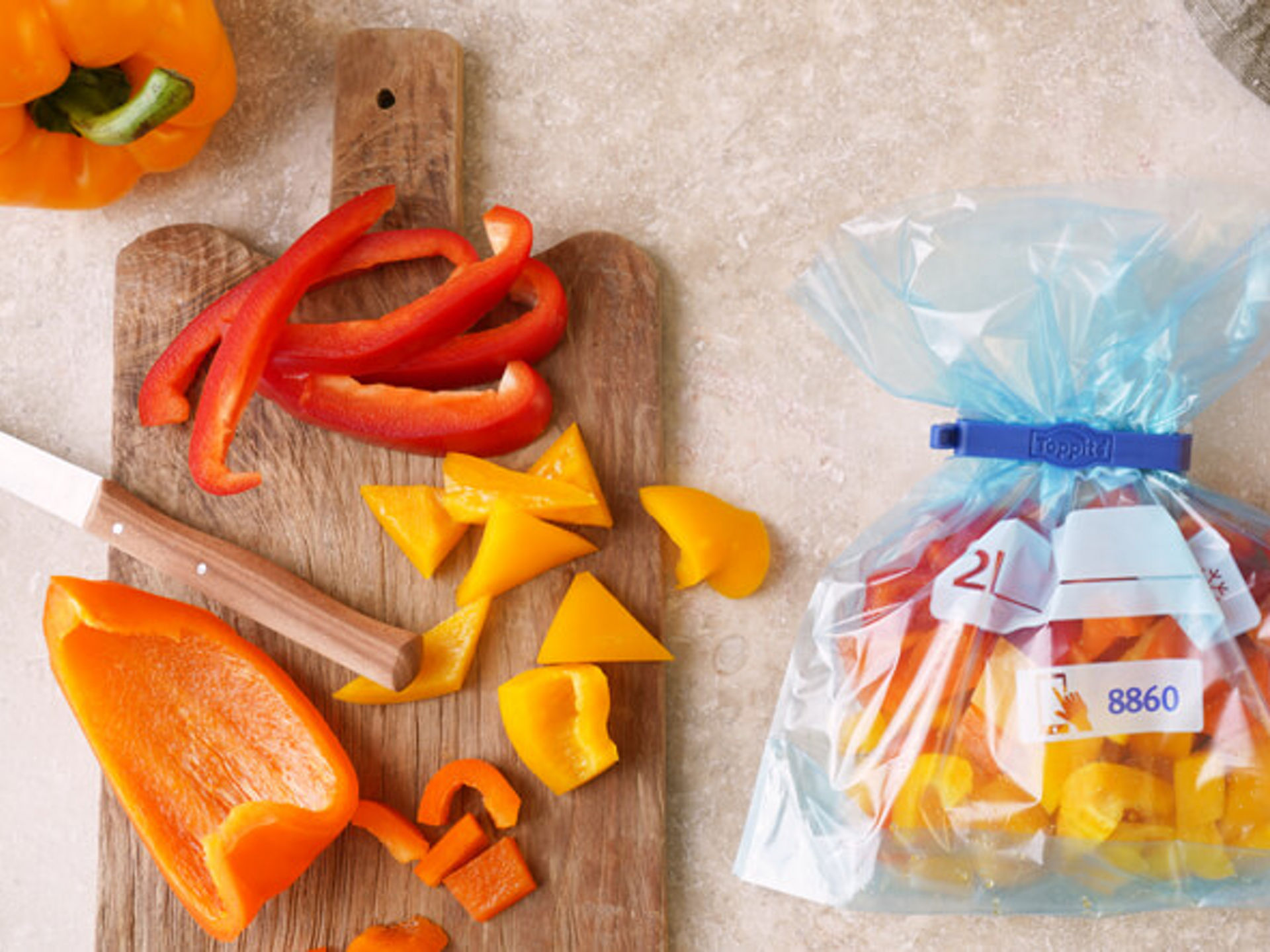 Paprika_einfrieren_Header Bunte geschnittene Paprika in einem Toppits Gefrierbeutel mit Klipp außen verteilt liegen Paprikastreifen und ein Messer