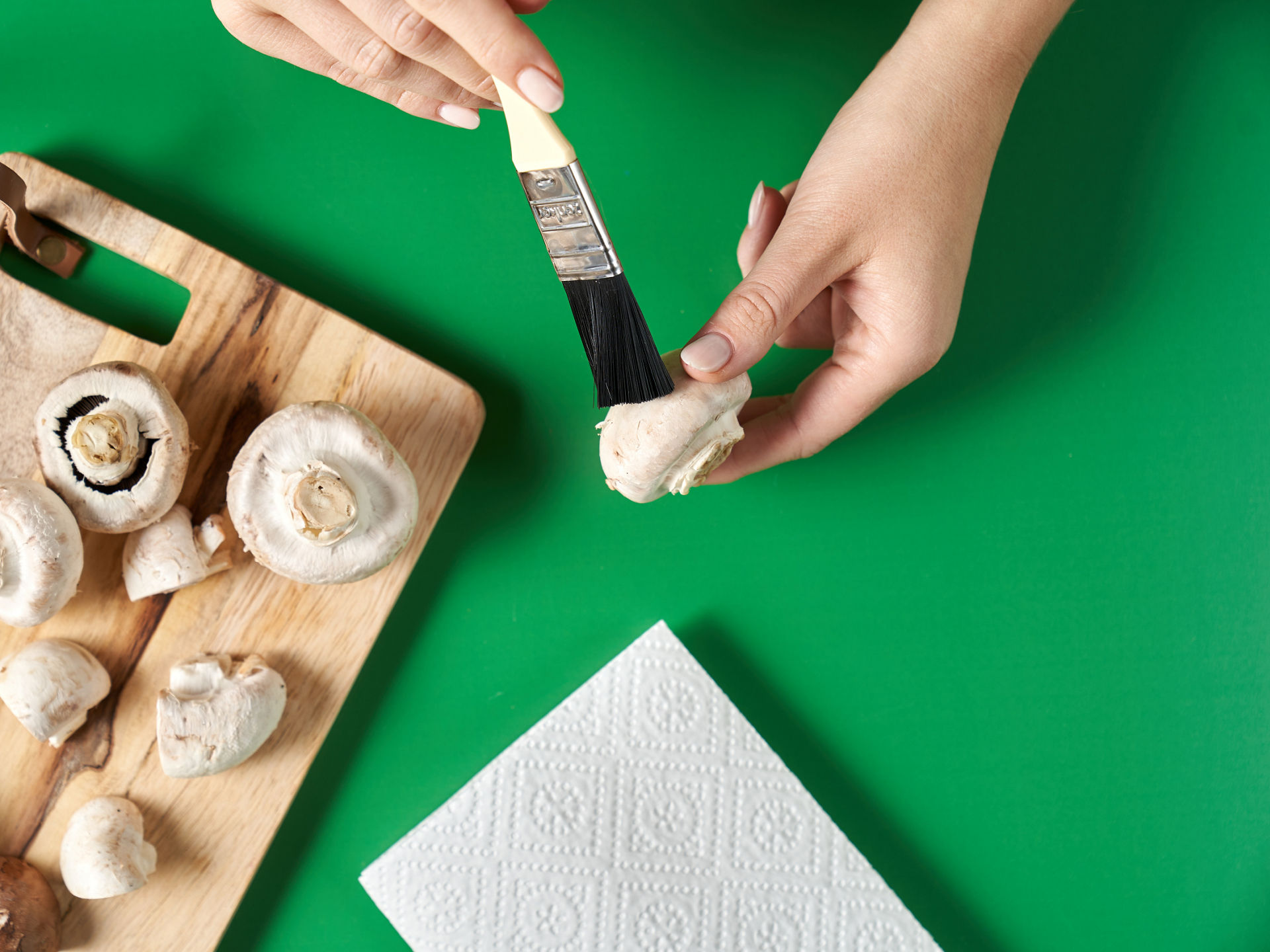 Frische Champignons werden mit einem Pinsel auf Holzbrett vorsichtig gereinigt.