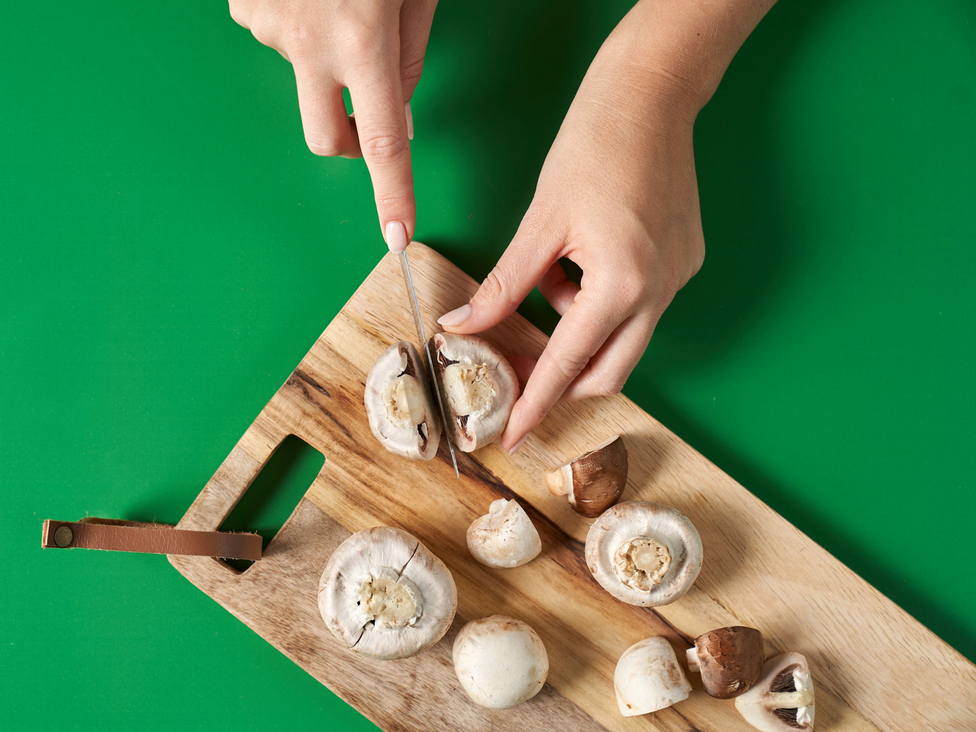 Champignons werden auf einem Schneidebrett in gleichmäßige Stücke geschnitten.