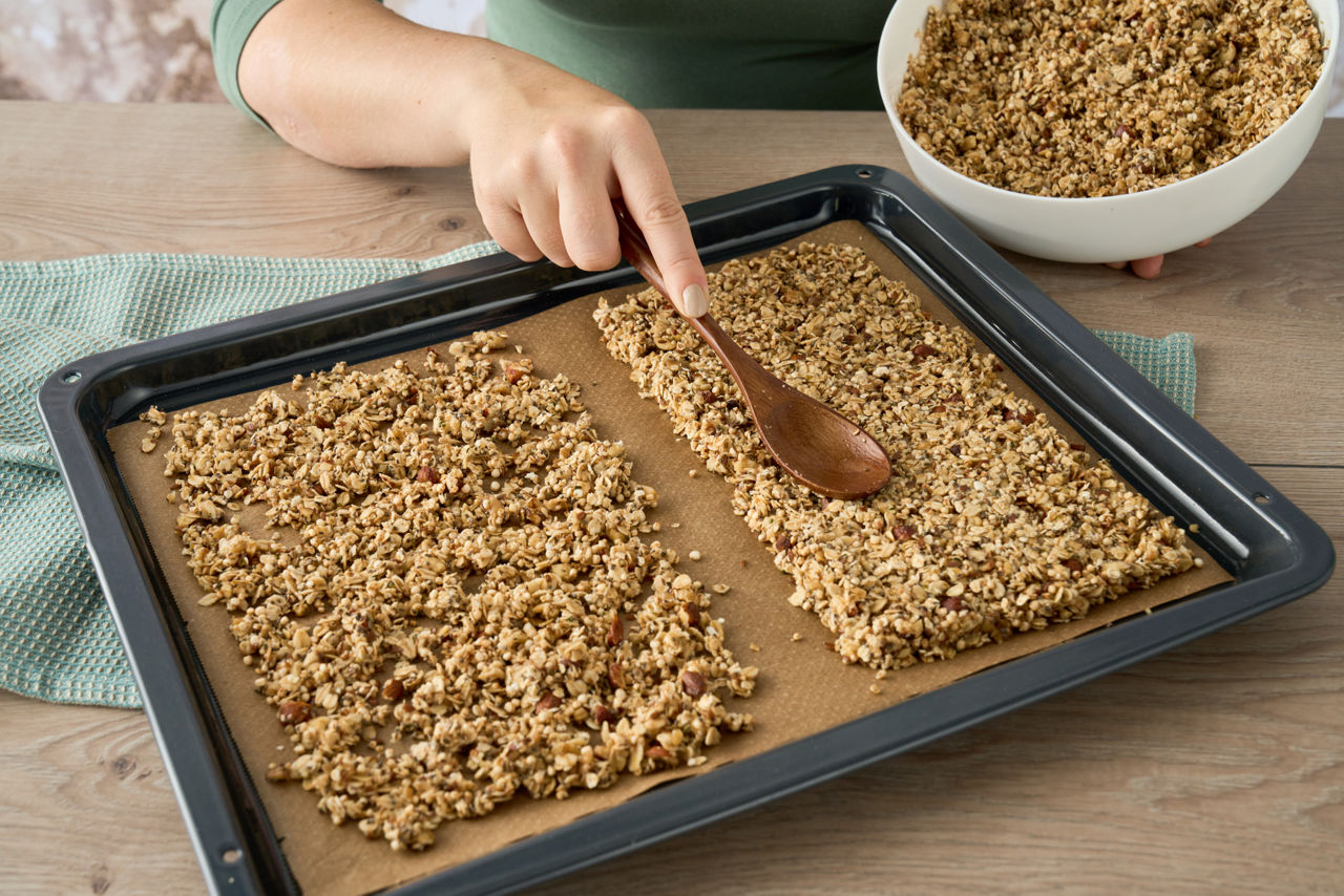 En person breder ut en klibbig deg med en träsked på Toppits® bakplåtspapper på en bakplåt.  Generated with AI