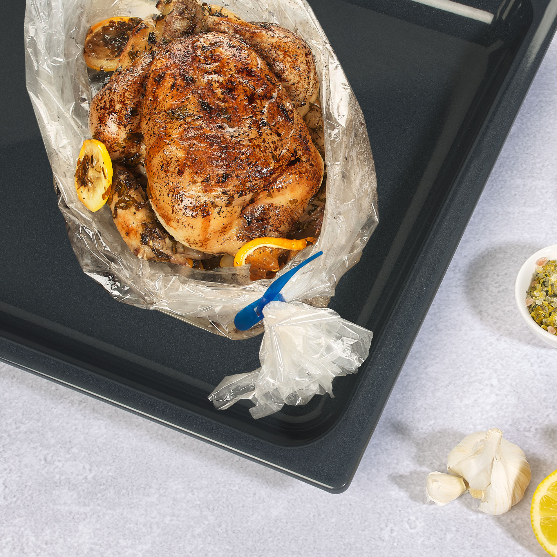 Poulet rôti dans sac de cuisson au four sur plaque de cuisson avec ramequins, citron et ail