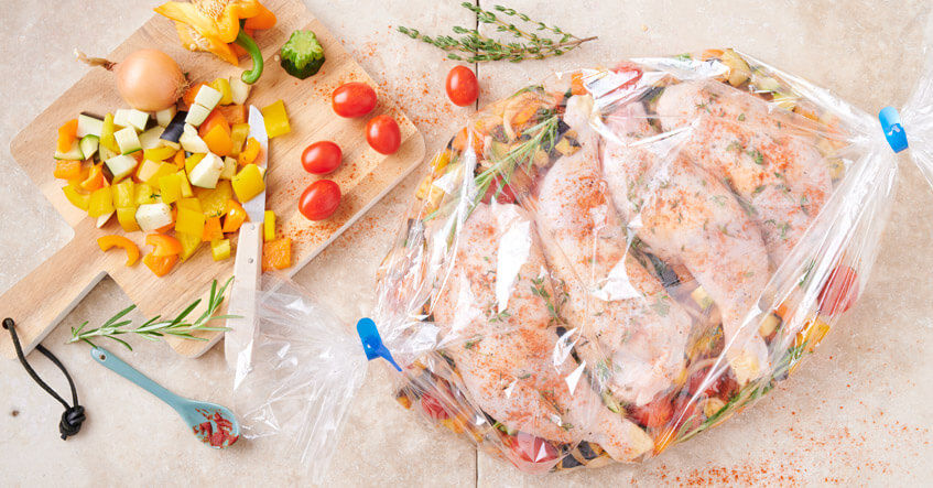Cuisses de poulet assaisonnées et petits légumes dans sac de cuisson fermé pour cuisson au four