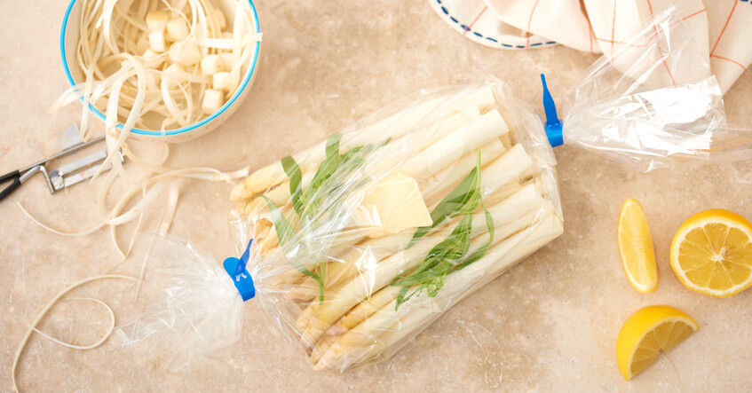 Asperges blanches épluchées dans un sac de cuisson fermé entouré de citrons et d'épluchures
