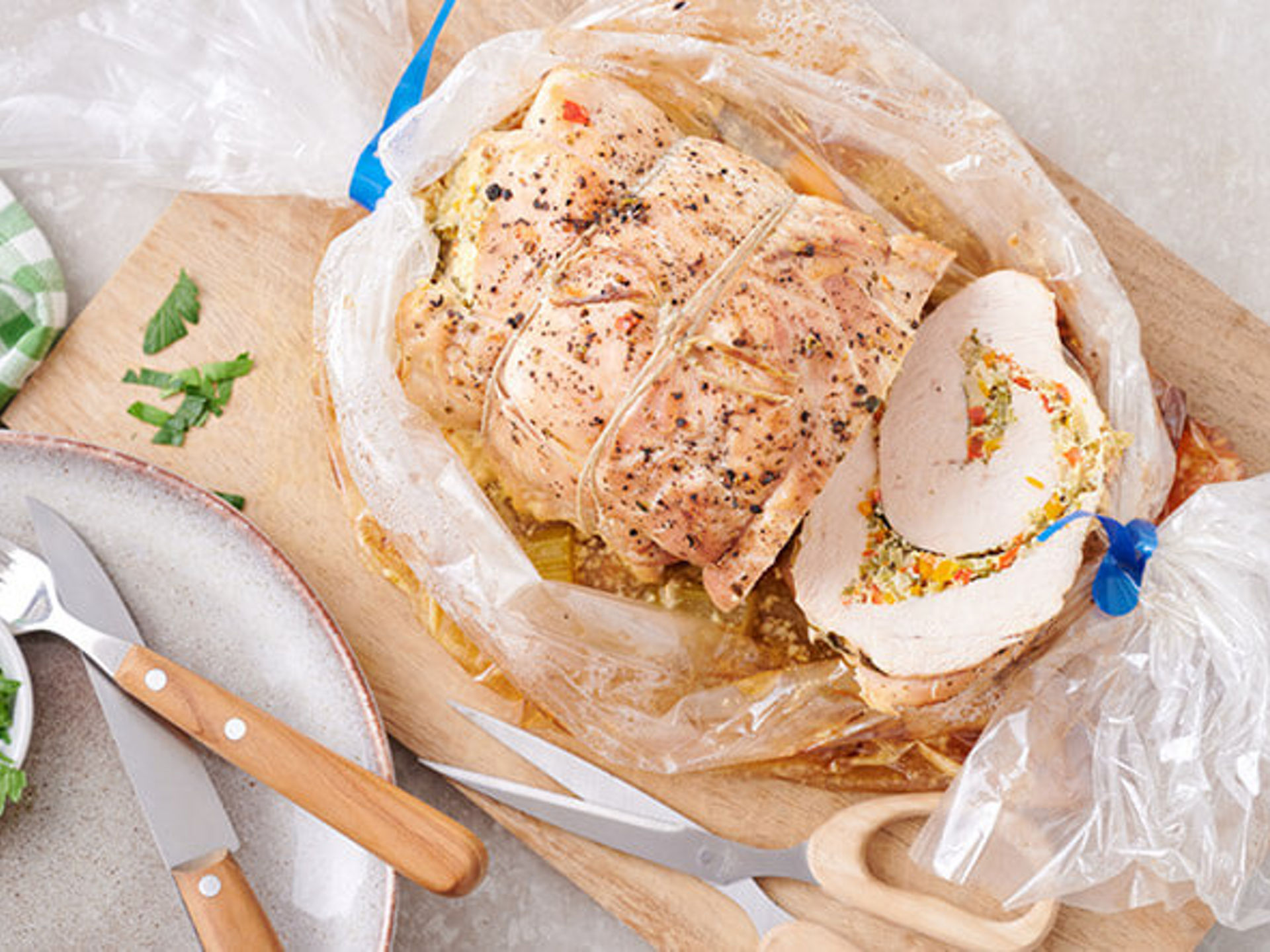 Rôti roulé cuit dans sac de cuisson découpé avec farce aux petits légumes et jus sur une planche