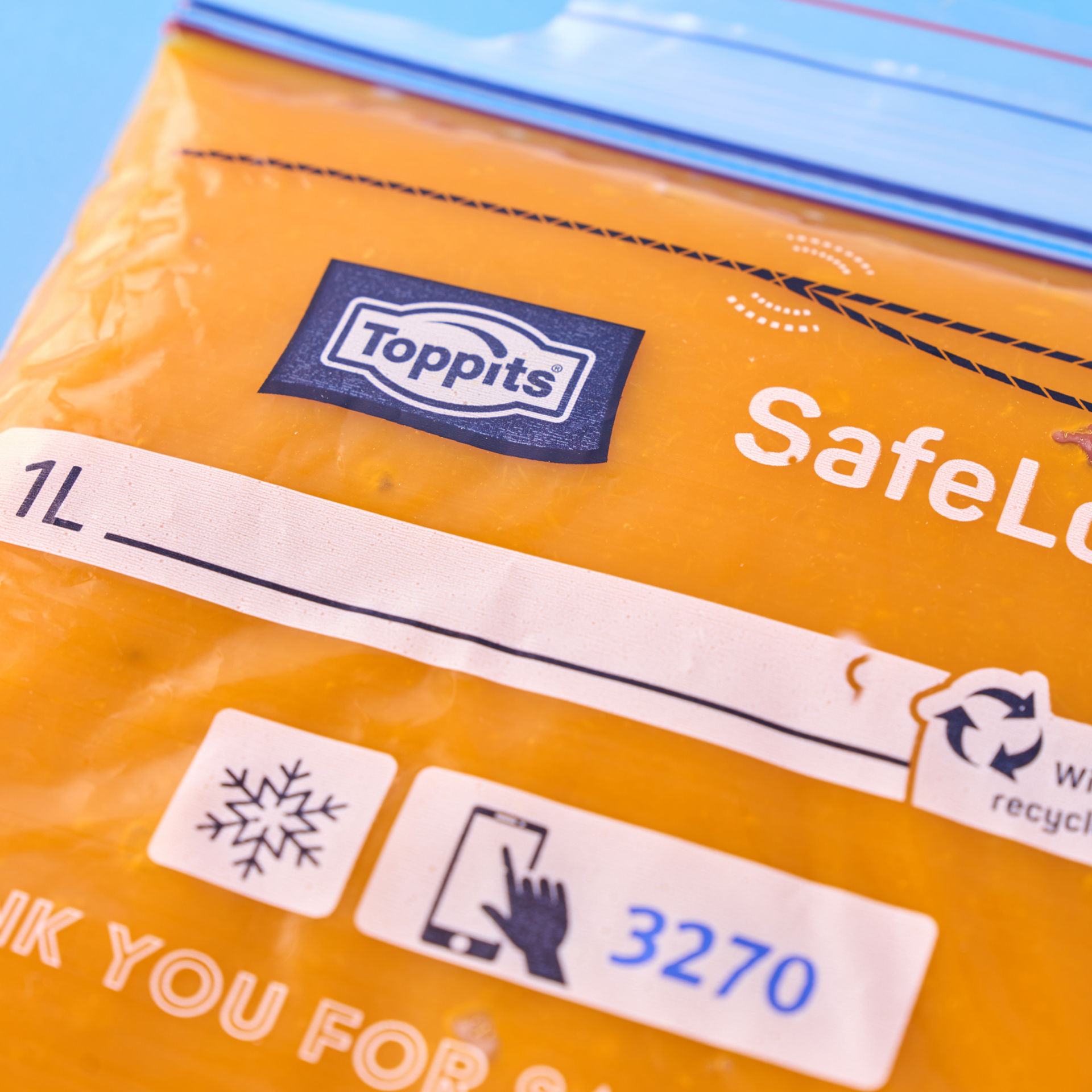 Nahaufnahme eines gefüllten Toppits SafeLoc Beutels mit orangener Flüssigkeit auf blauem Hintergrund.