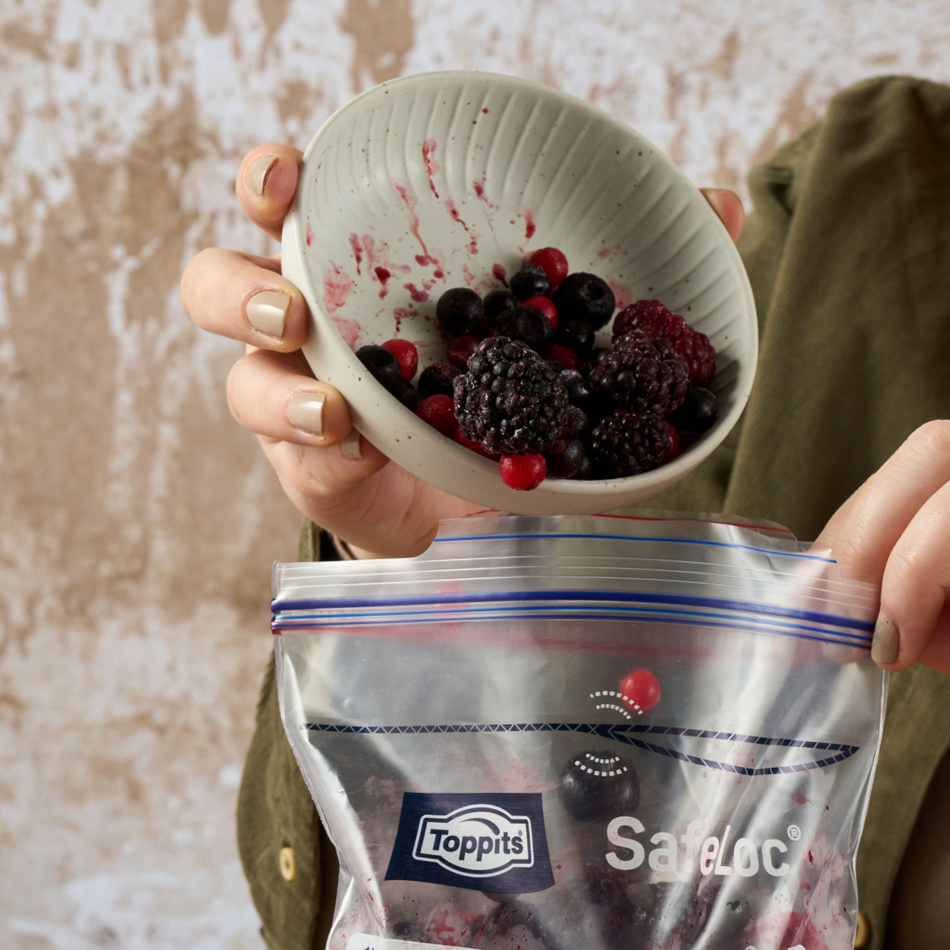 Toppits SafeLoc Beutel wird mit gefrorenen Beeren befüllt, eine Person hält Schüssel und Beutel.