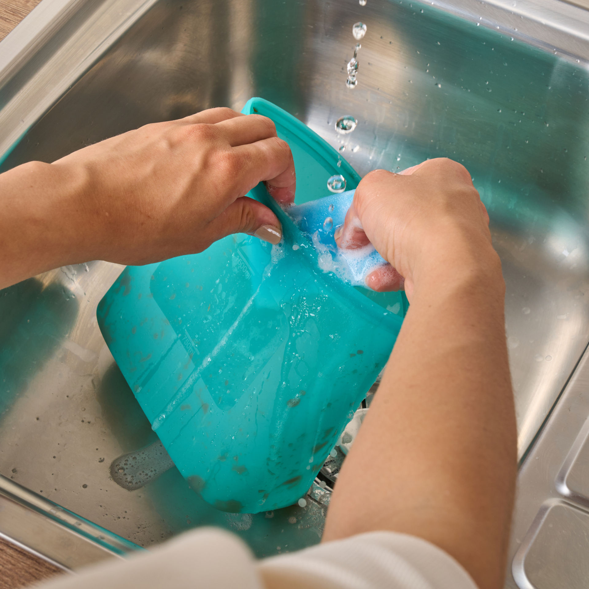 Person wäscht einen wiederverwendbaren Silikonbeutel unter fließendem Wasser in der Spüle.