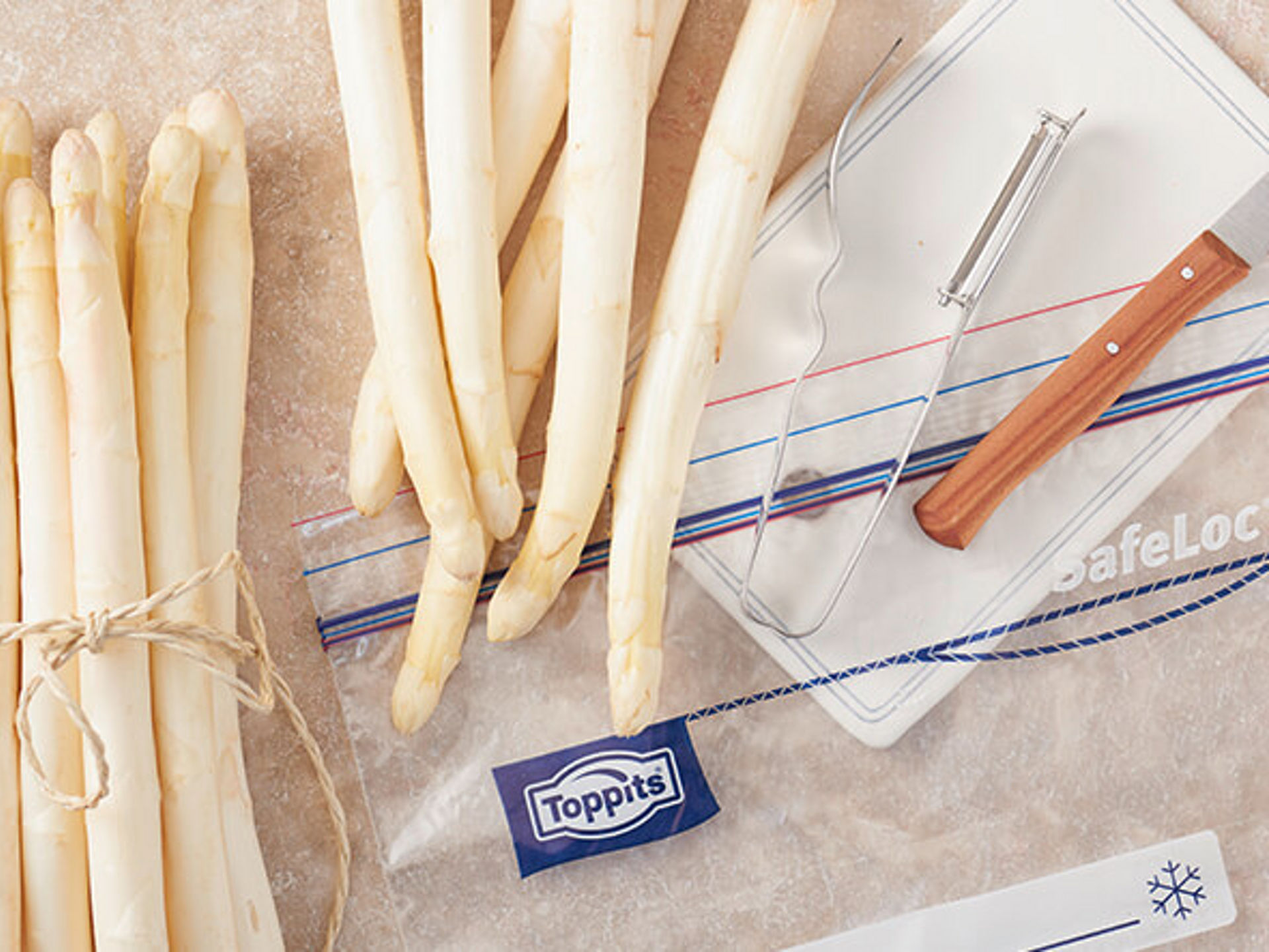 Frischer weißer Spargel, Sparschäler und Toppits SafeLoc Beutel auf Arbeitsfläche.