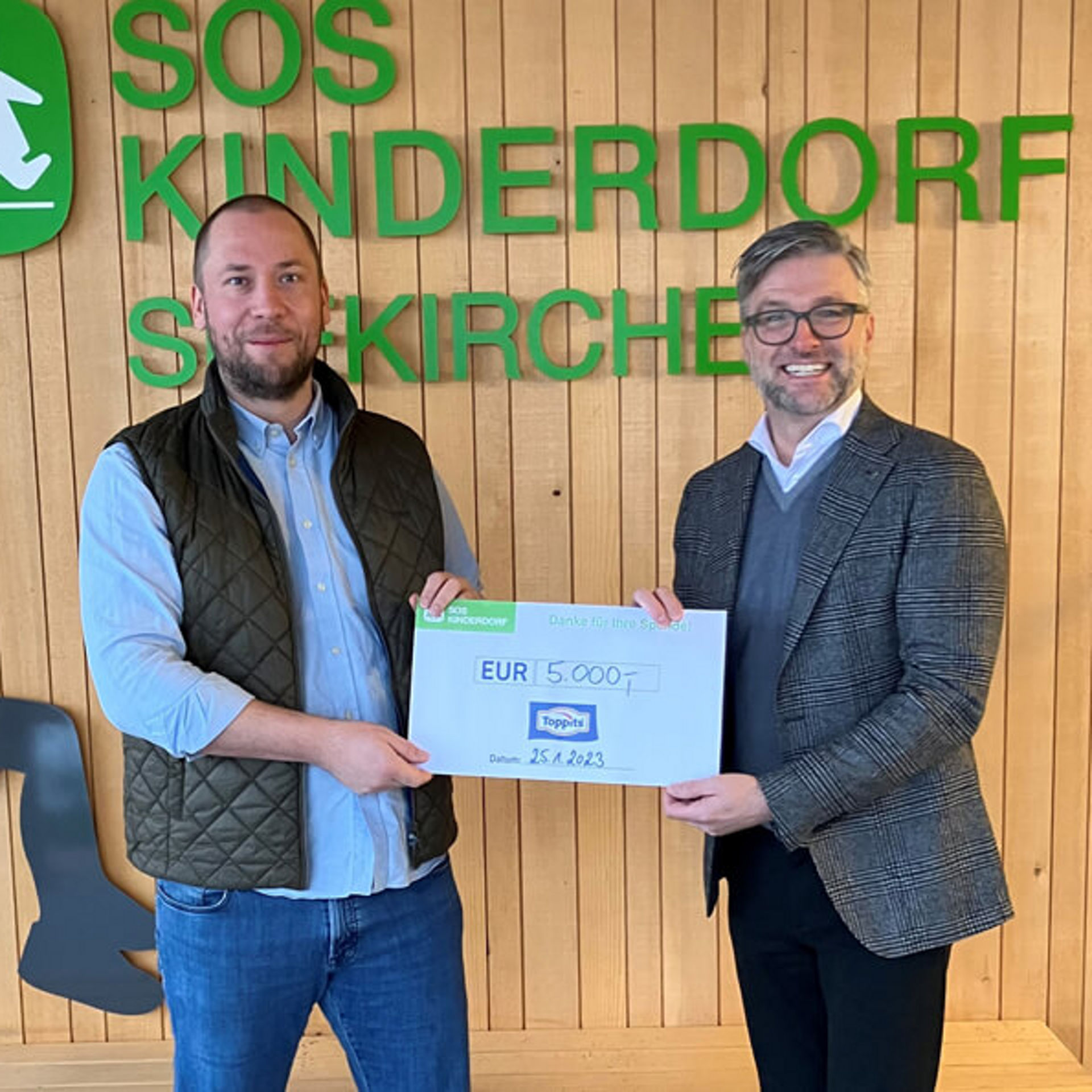 Zwei Personen übergeben einen großen Spendenscheck im SOS-Kinderdorf.