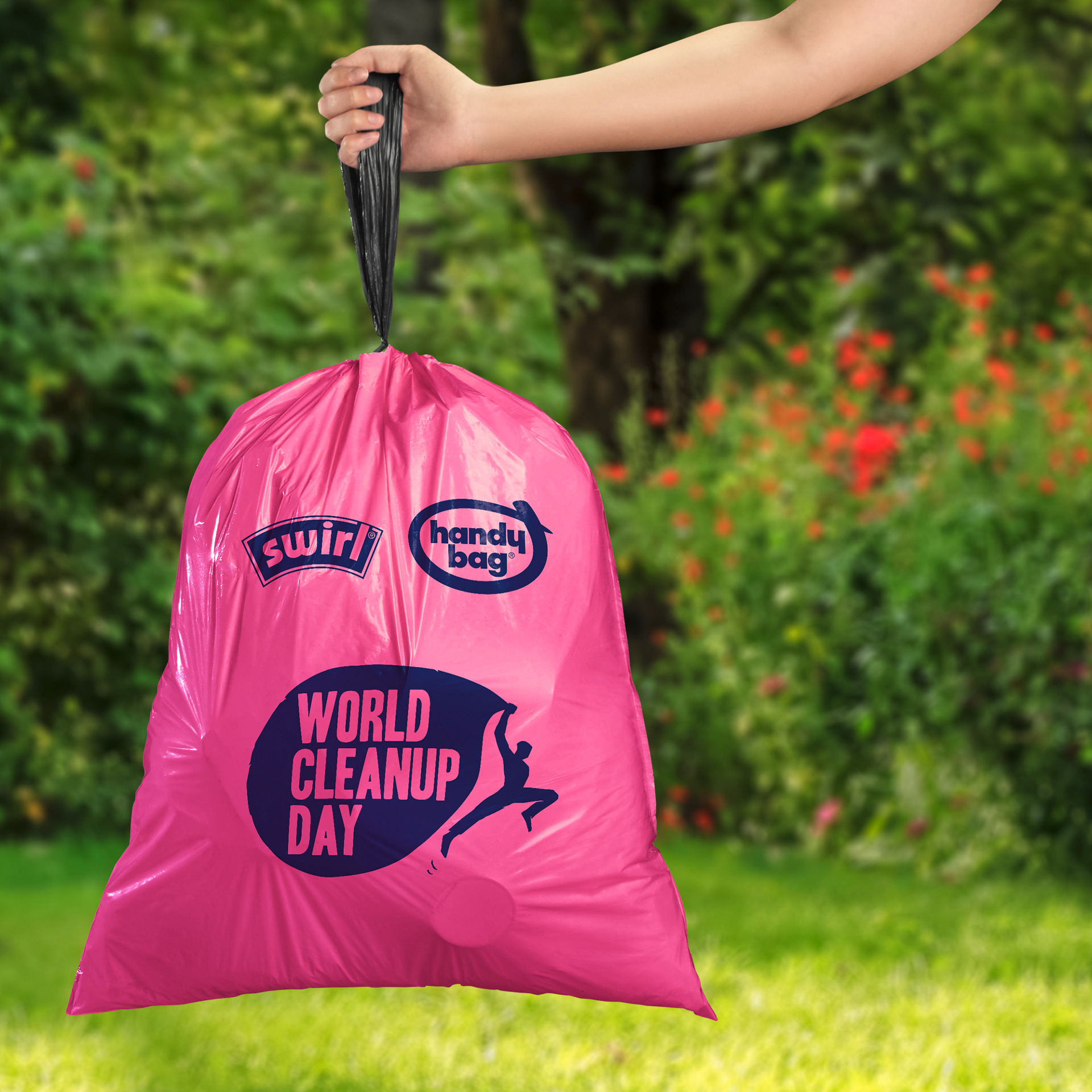 Ein pinker Swirl Handy Bag vollen Müllbeutel mit World Cleanup Day Aufdruck wird im Garten an einer Hand hochgehalten