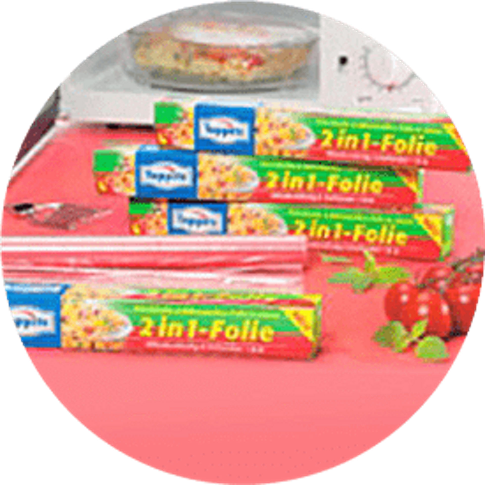 Toppits 2in1-Folie Verpackungen auf rotem Untergrund umgeben von Tomaten und Basilikumblättern. Im Hintergrund eine Tür offenstehende weiße Microwelle mit einem Gericht  innen drinnen 2002