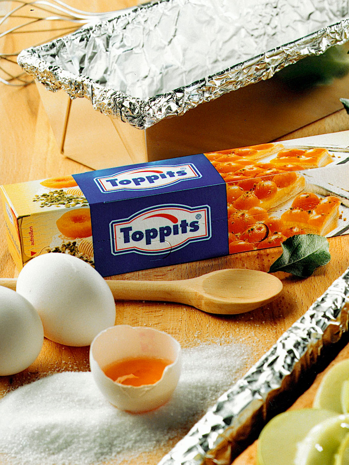 Eine Packung Back-Alufolie, ein Blechkuchen und ein Kastenkuchen liegen auf einem Tisch zusammen mit Lebensmitteln