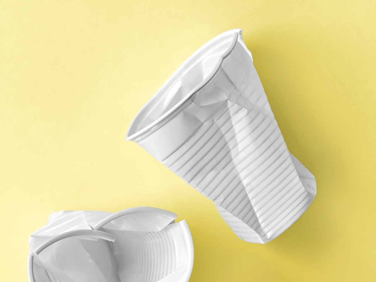 Weiße Einweg-Plastikbecher auf pastellgelbem Untegrund