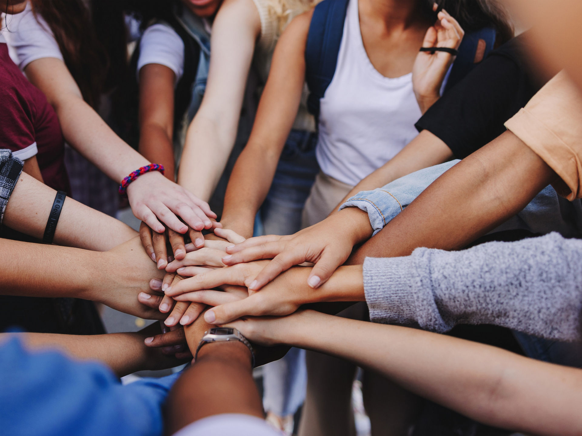 Gruppe von im Kreis stehenden Menschen legen ihre Hände in der Mitte zusammen