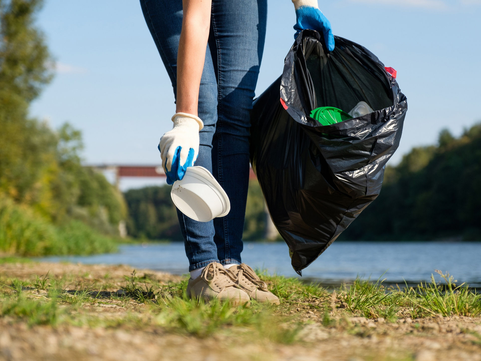Plastikmüll wird vom Boden aufgesammelt und einen schwarzen Müllbeutel verstaut