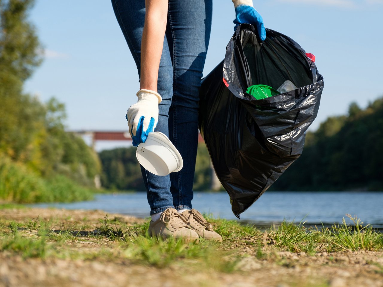 Plastikmüll wird vom Boden aufgesammelt und einen schwarzen Müllbeutel verstaut