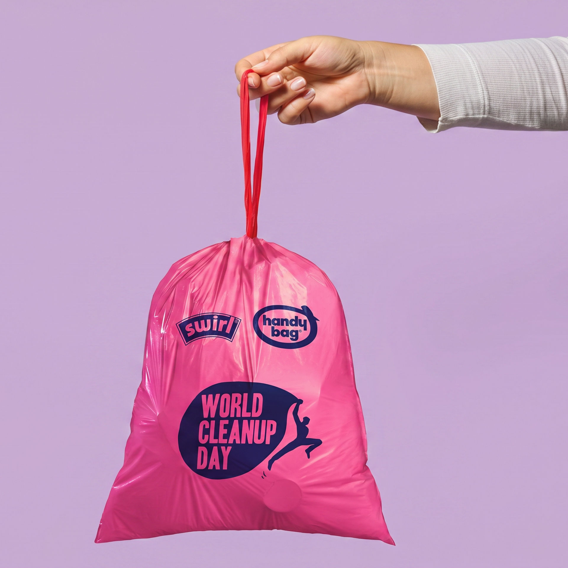 Hand hält einen zugebundenen pinken World-Cleanup-Day-Müllbeutel vor lila Hintergrund