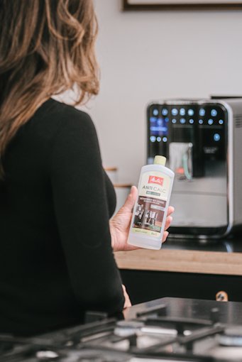 descale-11.png – Melitta® user interacting with machine during descaling routine, product category: coffee machine maintenance –