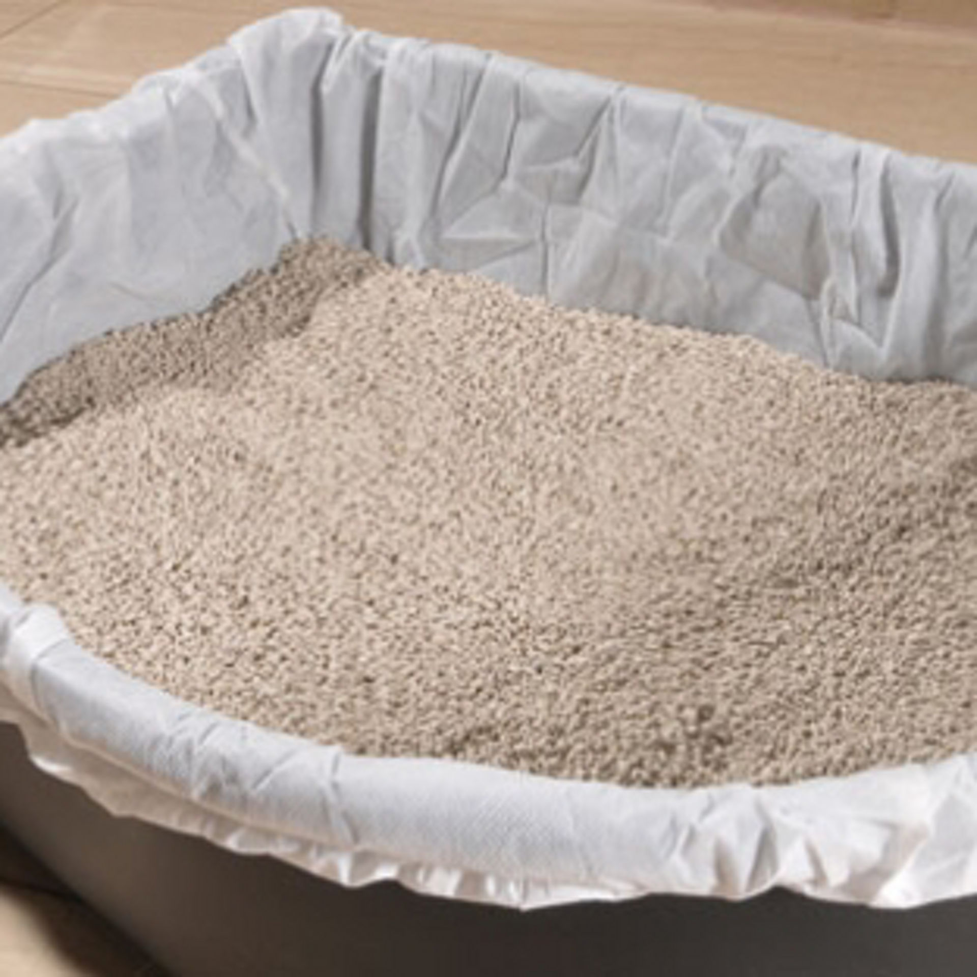 Bac à litière pour chat recouvert d’une housse de protection blanche, rempli de litière propre.