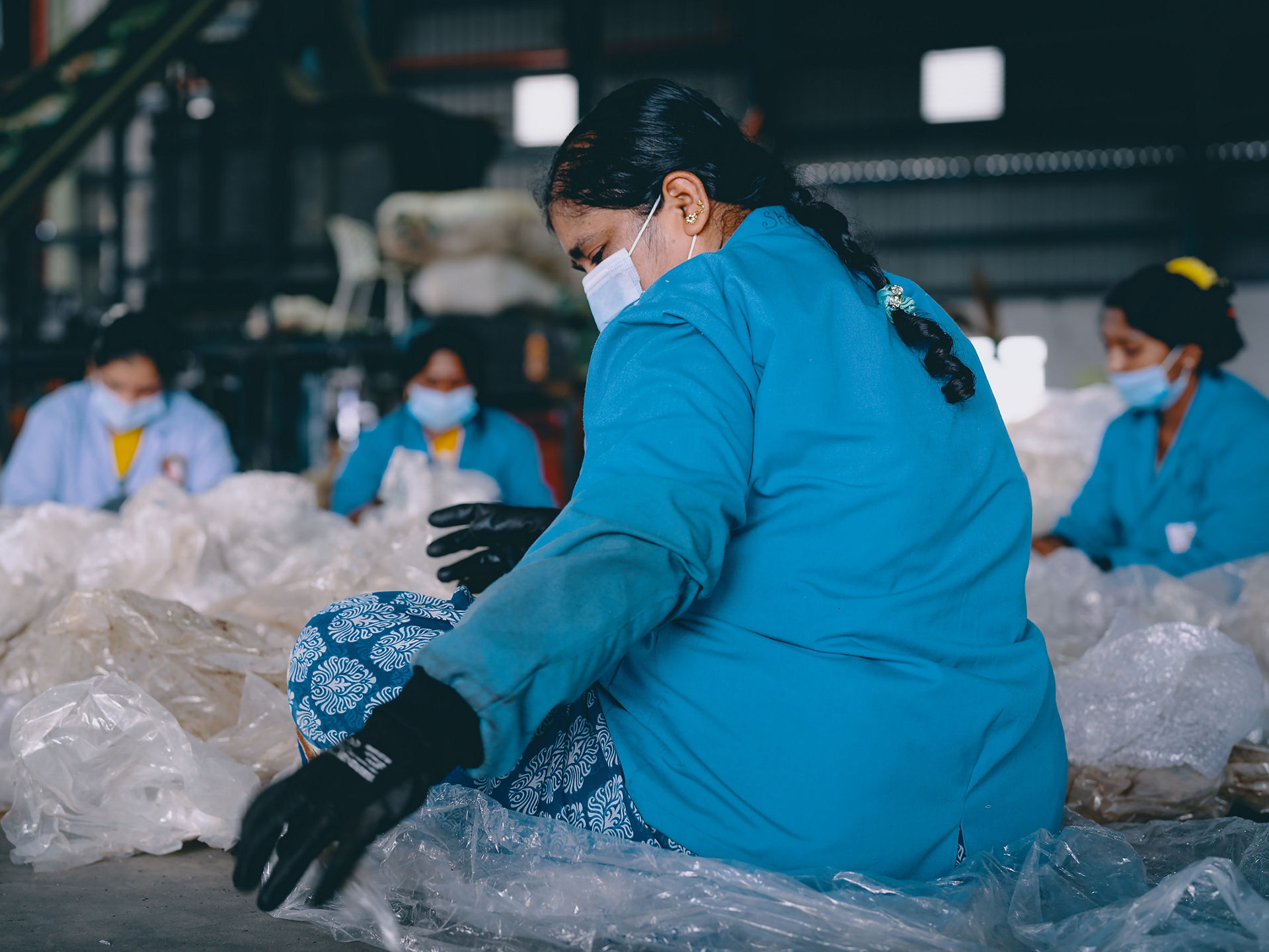 Frauen sortieren auf Boden sitzend altes Plastik in Recycling-Werk