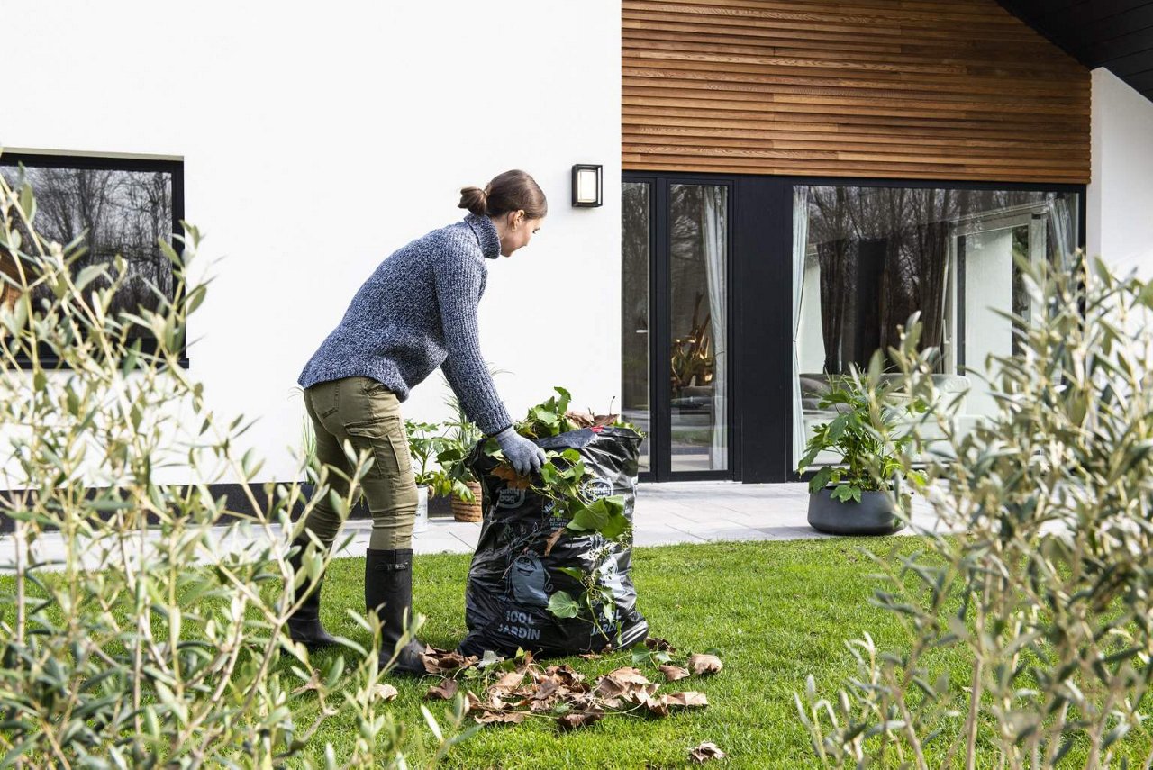 Femme charge un sac poubelle Handybag jardin 100 litres avec des feuilles vertes