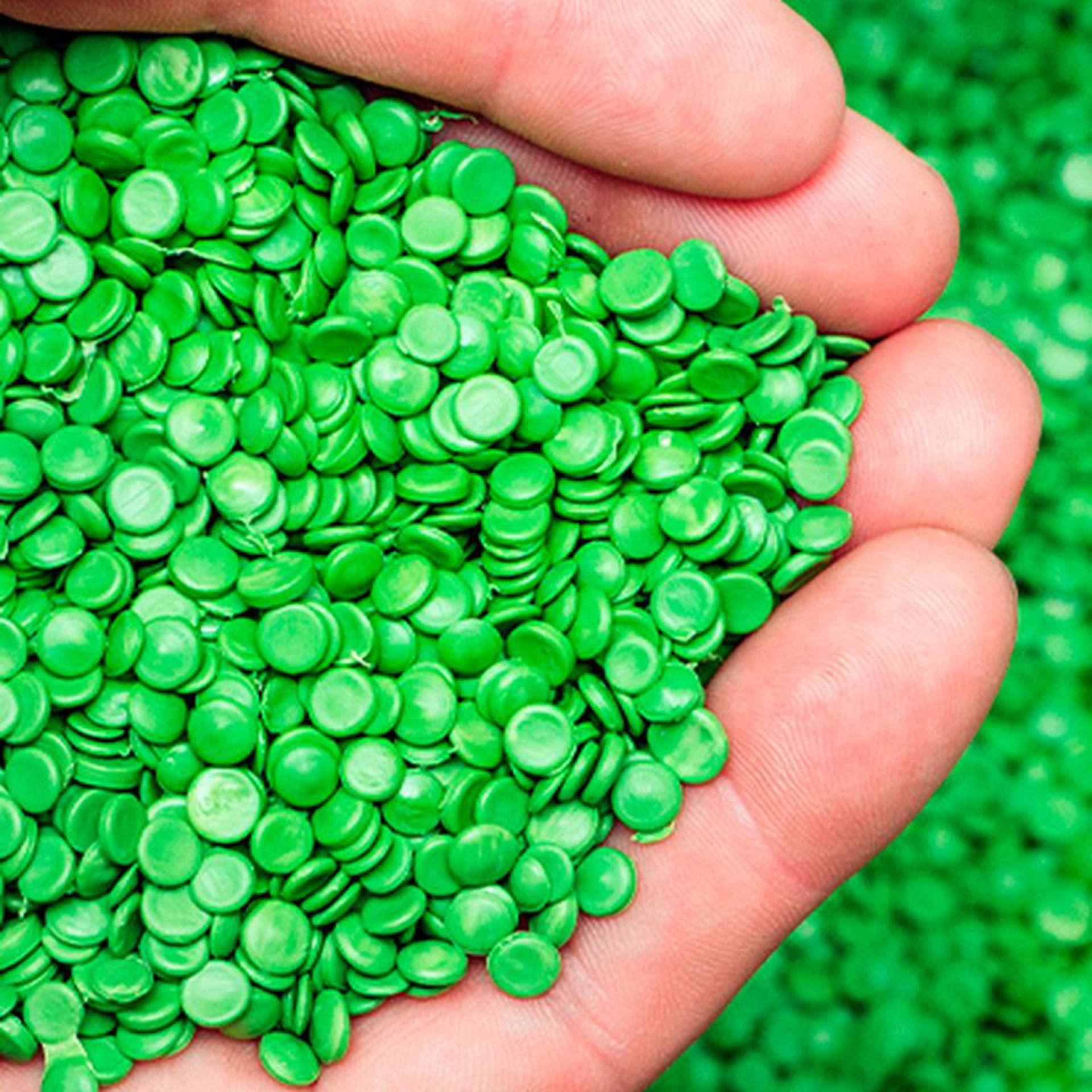 Mains tenant des granules de plastique vert recyclé