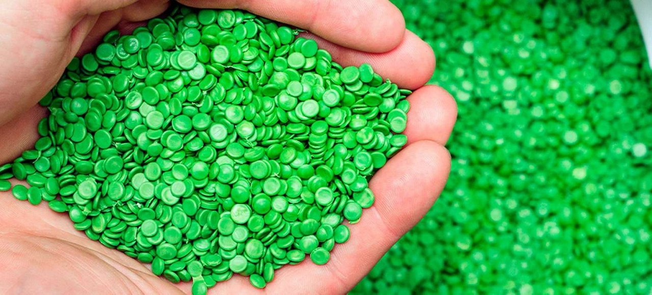 Mains tenant des granules de plastique vert recyclé