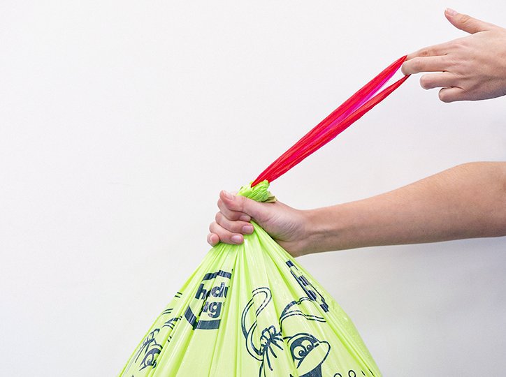 Mano cerrando una bolsa de basura Handybag verde con asas rosas