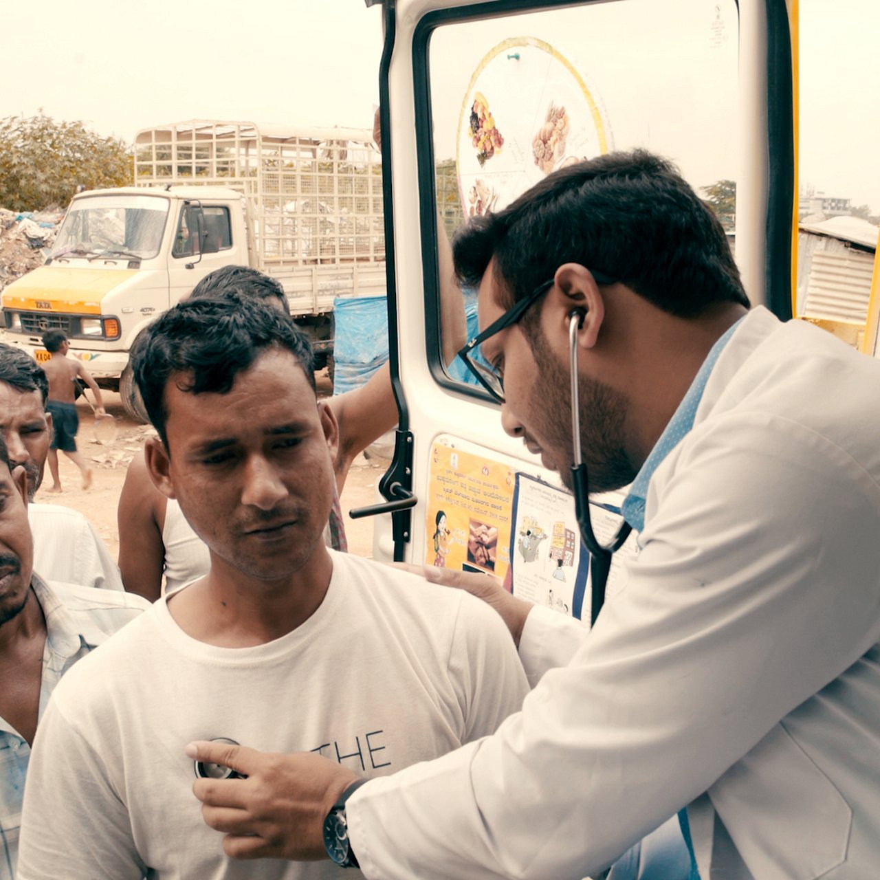 Professionnel de santé auscultant un homme près d’un camion et de déchets visibles