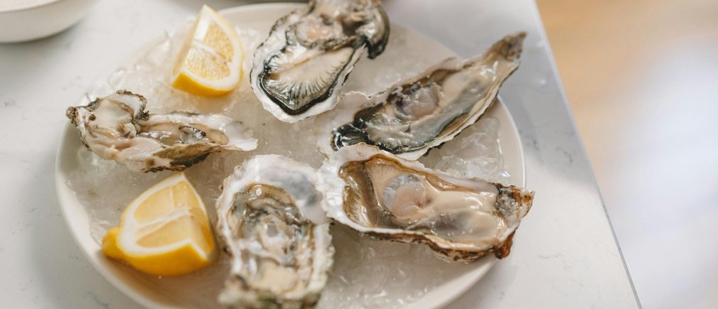 Ostras abiertas sobre una cama de hielo con gajos de limón y una mano